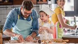 Ein Vater und sein Kind backen in der Küche, im Hintergrund sieht man die Mutter