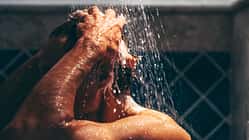 Engrossed in his grooming ritual, a man rinses his hair, the water's embrace enhancing the meditative quality of his daily routine.