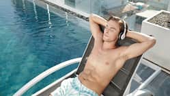 Junger Mann genießt ein Hörbuch am Pool