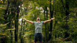 Mann steht im Wald und genießt mit offenen Armen die Natur und spürt Freiheit