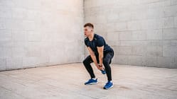 Sportlicher Mann in leerem Raum führt eine Hip Hinge Übung mit einem Kettle Ball aus