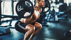 Sportlicher Mann macht oberkörperfrei eine Squatübung mit einer Langhantel im Fitnessstudio