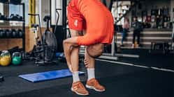 Ein junger Mann in orangener Sportkleidung dehnt sich vor dem Training im Fitnessstudio.
