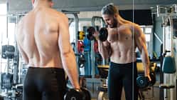 Mann steht beim Gewichtheben im Gym vorm Spiegel Mann steht beim Gewichtheben im Gym vorm Spiegel