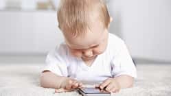 Ein Baby liegt auf dem Fußboden und spielt an einem Smartphone
