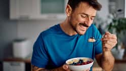 Ein Mann im blauen Sportshirt isst glücklich Haferflocken mit Obst aus einer Schale Ein Mann im blauen Sportshirt isst glücklich Haferflocken mit Obst aus einer Schale