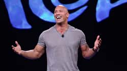 Dwayne Johnson im blaugrauen Shirt mit ausgebreiteten Armen, der auf der Premiere von "Moana" in die Kamera lacht