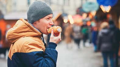 Mann mit Mütze isst auf dem Weihnachtsmarkt eine süße gefüllte Blätterteigrolle