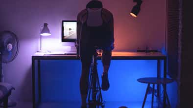 Mann fährt im Arbeitszimmer vor dem Laptop auf einem Indoor Cycle