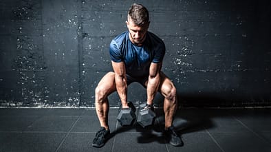 Mann hält im Squat zwei schwere Kurzhanteln und ist im Begriff, sie hochzustemmen