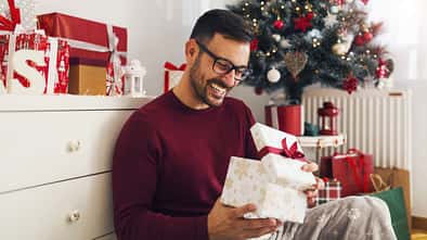 Smiling,Young,Man,Opening,Christmas,Gift,At,Home
