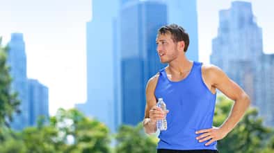 Männlicher Läufer steht schwitzend vor New Yorker Skyline mit einer Wasserflasche. 