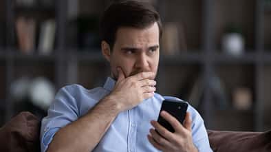 zweifelhafter Mann sitzt auf dem Sofa und schaut von seinem Smartphone auf