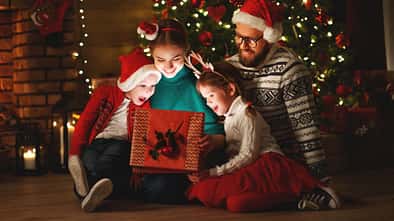 Familie schaut in ein Geschenk unter dem Tannenbaum.