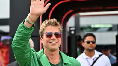 Brad Pitt hebt die Hand und lächelt in die Kamera