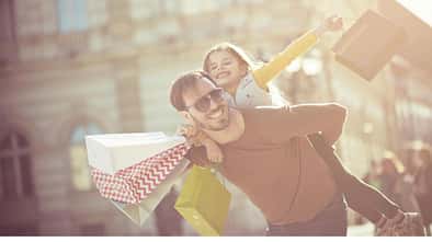 Ein Vater trägt seine mit Einkaufstaschen beladene kleine Tochter auf dem Rücken