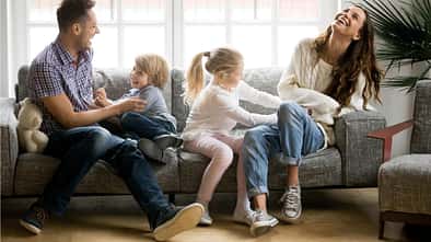 Mutter und Vater sitzen mit ihren zwei Kindern auf dem Sofa und albern herum