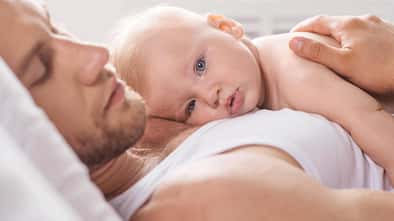 Ein Vater liegt im Bett und hat sein Baby auf der Brust
