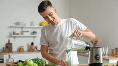 Junger Mann bereitet grünen Smoothie zu