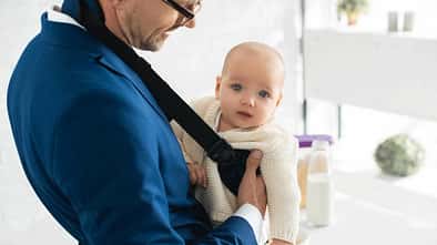 Ein Vater trägt sein kleines Kind in einer Babytrage vor der Brust