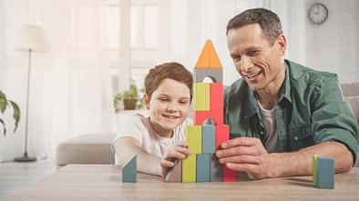 Ein Vater sitzt am Tisch und spielt mit seinem Sohn mit Bauklötzen