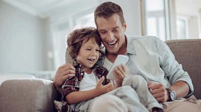 Vater und Sohn sitzen auf dem Sofa und amüsieren sich mit einem Smartphone