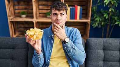 Mann guckt skeptisch auf Schüssel mit Chips
