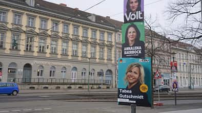 Man sieht eine Straße an der drei Wahlplakate stehen