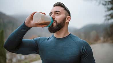Ein junger Sportler trinkt draußen einen Protein-Shake