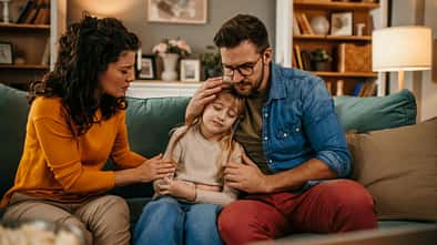 Mutter und Vater sitzen auf dem Sofa und trösten ihre traurige Tochter
