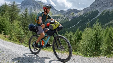 Man bikepacking, he cycles through the mountains and pine tree forests