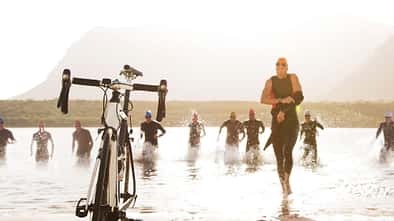 Triathleten laufen durch das Wasser zu ihren Fahrrädern