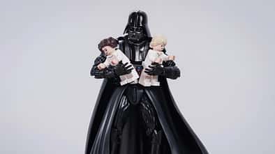 Darth Vader hält zwei übergroße Legofiguren von Leia und Luke im Arm