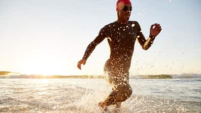 Mann rennt in Neoprenanzug und Schwimmbrille durchs Wasser