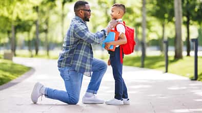 Ein Vater kniet vor seinem Sohn und macht ihn fertig für die Schule