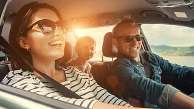 Frau und Mann sitzen gutgelaunt im Auto, auf der Rückbank sieht man ein fröhliches Kind.