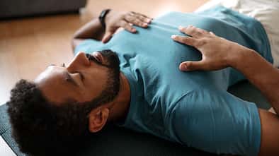 The single man meditating alone at home, doing breathing exercises. Concentrate on deep breathing, holding his chest, doing hand mudra or hand gesture technique.