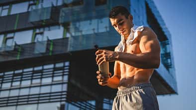 Ein junger Mann trinkt oberkörperfrei einen Proteinshake