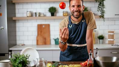 Portrait von einem Mann, der kocht und eine Tomate in die Luft wirft