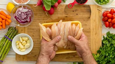 Geflügelfleisch auf einem Holzbrett, Gemüse liegt an der Seite
