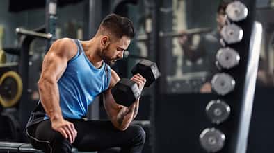 Bodybuilder,Pumping,His,Biceps,With,Dumbbell,In,Gym,,Empty,Space