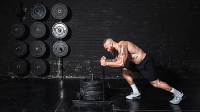 Junger fitter Mann schiebt schwere Hantelscheiben auf dem Prowler Schieber 