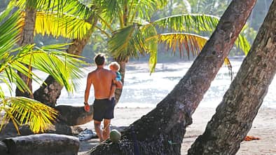 Ein Vater steht mit seinem kleinen Kind auf dem Arm an einem Strand in der Karibik 