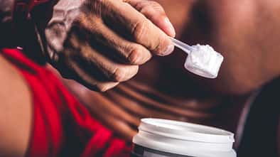 Ein Mann nimmt einen Scoop Kreatinpulver aus einer Dose