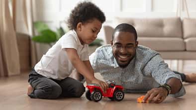 Ein Vater liegt mit seinem kleinen Sohn auf dem Wohnzimmerboden und spielt mit Autos