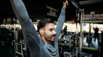 Young sportsman stretching back muscles while listening music in gym