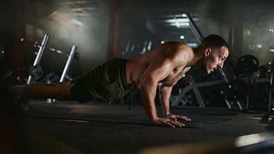 Muscular build men exercising push-ups in a gym.