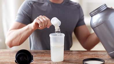 Ein Mann, der sich einen Scoop Kreatin-Pulver in seinen Shaker füllt