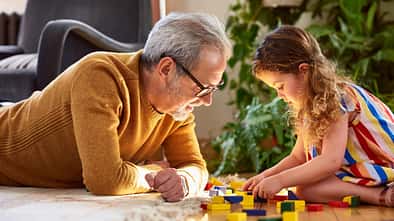 Ein Vater und sein Kind liegen auf dem Fußboden und spielen mit Bauklötzen
