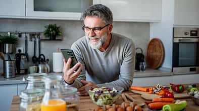 Ein Mann schaut auf sein Handy und kocht gesund